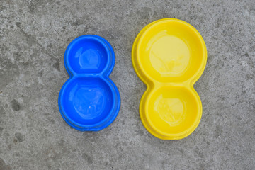 Two double plastic pet bowls in blue and yellow. Empty bowls on concrete background. View from above.