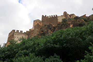 Fototapeta na wymiar Walls and towers of old medieval Sagunto impregnable fortress ruin on a hill in Spain surrounded by green forest