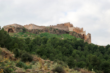 Fototapeta na wymiar Walls and towers of old medieval Sagunto impregnable fortress ruin on a hill in Spain surrounded by green forest