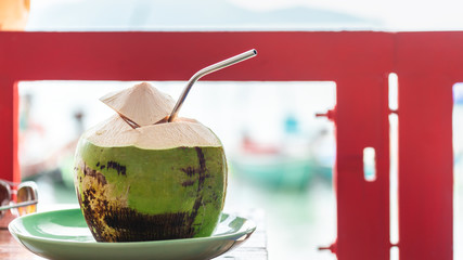 Fresh and cold whole coconut served with cut top and straw inside in beach side cafe, Koh Samui, Thailand