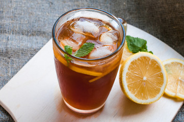 Black iced tea in a glass, next to lies a yellow sliced lemon on a wooden board. The concept of healthy eating.