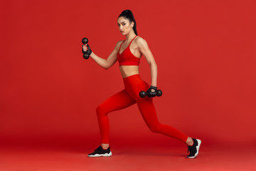 Fototapeta na wymiar Confidence. Beautiful young female athlete practicing in studio, monochrome red portrait. Sportive fit brunette model with weights. Body building, healthy lifestyle, beauty and action concept.