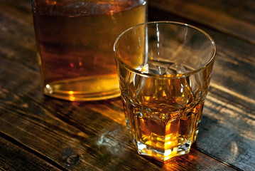 A glass of alcohol near a bottle. Old whiskey bottle on black wooden table. Drinks on a dark blurred background.