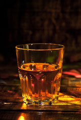 A glass of alcohol near a bottle. Whiskey on a black wooden table. Drinks on a dark blurred background.