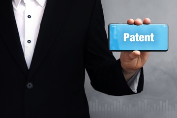 Patent. Geschäftsmann im Anzug hält ein Smartphone in die Kamera. Der Begriff Patent steht auf dem Handy. Konzept für Business, Finanzen, Statistik, Analyse, Wirtschaft