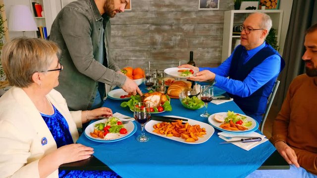 Zoom in shot of man serving his father with chicken at family dinner.
