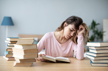 Upset young woman with books sit at work desk.