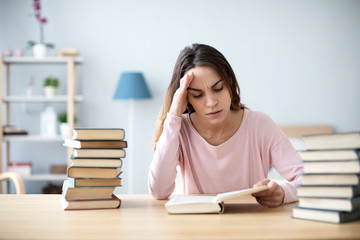 Sad female student reading a book for the exam or doing homework.