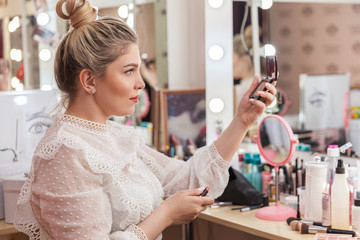 The magnificent blonde paints lips at a make-up mirror