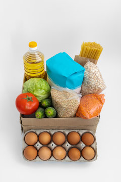 Food donations box isolated on gray background. Cabbage, cucumber, tomatoes, flour, sunflower oil, spaghetti, oatmeal, lentils, eggs in box.