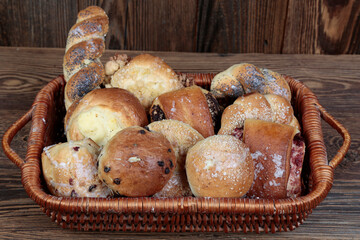 Fresh, natural, homemade bread, rolls, croissant, buns in a wicker basket on a wooden, brown, rustic table.