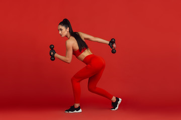 Fototapeta na wymiar Graceful. Beautiful young female athlete practicing in studio, monochrome red portrait. Sportive fit brunette model with weights. Body building, healthy lifestyle, beauty and action concept.