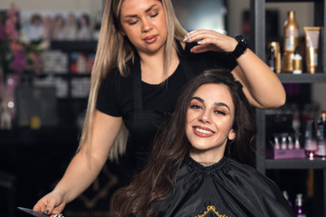 Female hairdresser makes hairstyle on young woman with brunette hair in salon.	