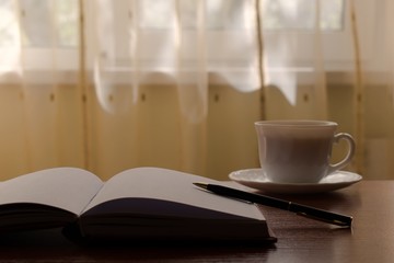 pen with a diary and a cup of tea on the table on a sunny morning