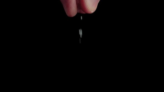 Professional chef sprinkles a ready-made dish with salt. Sea salt drops on fresh ingredients of something on a black board against black background. Extremely close up. Slow motion