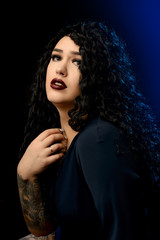 Portrait of a beautiful brunette girl with a tattoo in a dark dress against a black background with blue highlighter