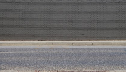Fototapeta premium Gray painted brick wall with concrete sidewalk and asphalt road in front. Background for copy space.