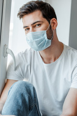 Fototapeta na wymiar Man in medical mask looking at camera near window