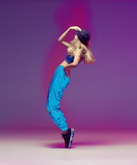 Cute teen girl dancing hip hop in reflective pants, baseball cap, in a Studio with neon lighting. Dance color poster.