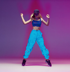 Cute teen girl dancing hip hop in reflective pants, baseball cap, in a Studio with neon lighting. Dance color poster.