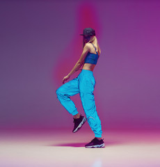 Cute teen girl dancing hip hop in reflective pants, baseball cap, in a Studio with neon lighting. Dance color poster.