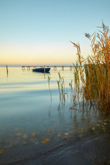 Fototapeta na wymiar Ruhiger See mit sanften Wellen, Schilf und einem dekorativen Steg und einem blauen Boot
