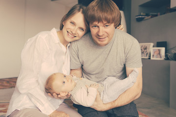 Cheerful positive new parents enjoying leisure time with baby daughter. Young couple holding six month child and looking at camera. Parenthood concept