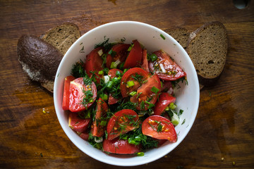 Tomato salad with olive oil and balsamic vinegar in bowl over wooden background
