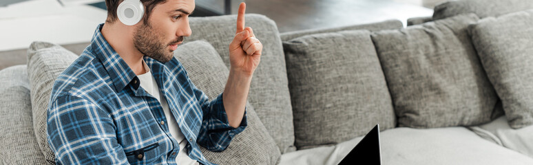 Panoramic crop of freelancer in headphones having idea while looking at laptop on sofa
