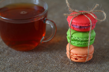 Macaroons multicolored and a glass cup of tea on a table with a burlap tablecloth