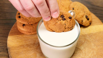 Hand Dipping a chocolate chip cookie in milk on wooden board. Close up.
