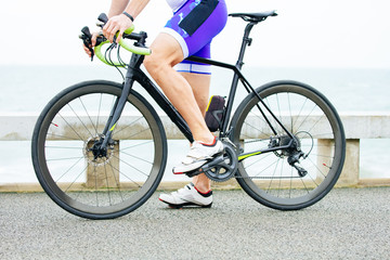 Partial view of man riding bicycle. Low section of sportsman in sneakers cycling on bike near body of water. Triathlon concept