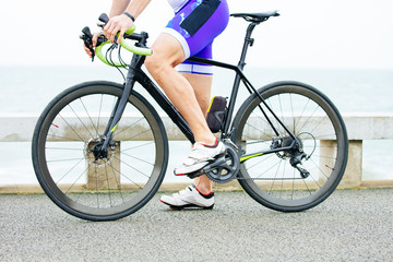 Naklejka premium Partial view of man riding bicycle. Low section of sportsman in sneakers cycling on bike near body of water. Triathlon concept