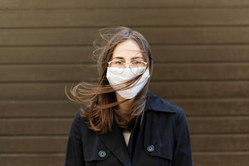 young woman in a protective medical mask against viruses and covid19 stands and her hair is playing...