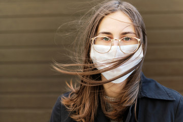 young woman in a protective medical mask against viruses and covid19 stands and her hair is playing in the wind.