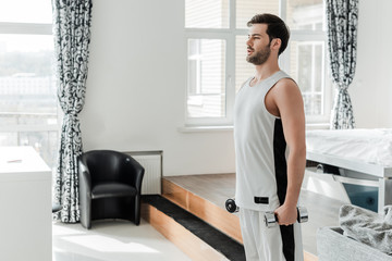 Fototapeta premium Handsome man holding barbells while training at home