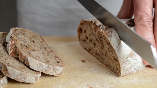 Hands cut organic sourdough bread with type 0 wheat flour, rye, spelled and various seeds of flax, sunflower, sesame and poppy.