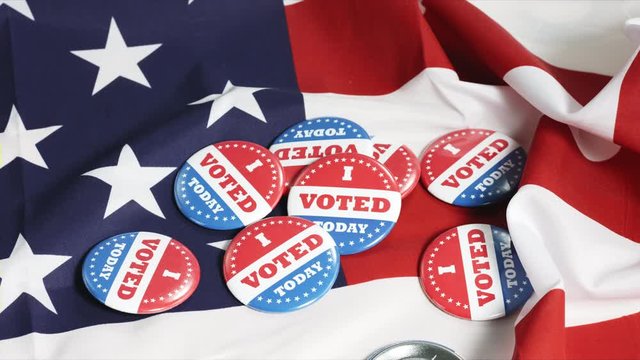 Buttons of I Voted Today for the US elections falling on american flag in background. slowmotion