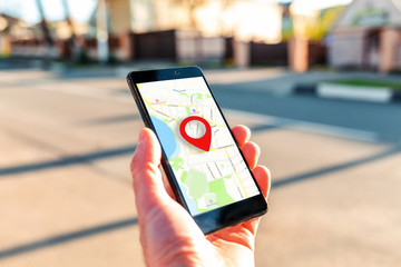 Male hand holding holding smartphone with online-a map on which the geolocation icon. In the...