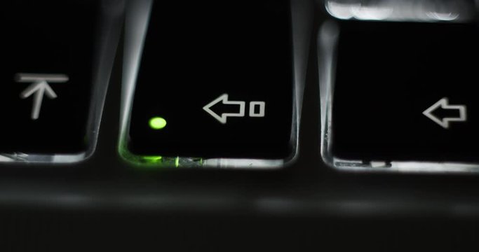 Pressing caps lock on backlit illuminated laptop computer keyboard at night