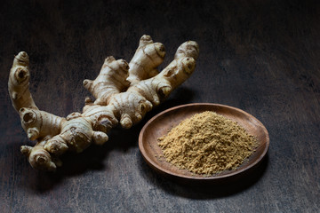 Fresh organic ginger root and powder in wooden bowl on dark old rustic background with copyspace.