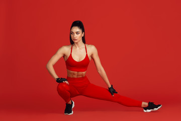 Fototapeta na wymiar Stretching. Beautiful young female athlete practicing in studio, monochrome red portrait. Sportive fit brunette model training. Body building, healthy lifestyle, beauty and action concept. Copyspace.