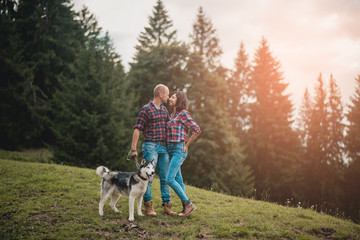 Romantic traveling couple walking with husky dog in the mountains. Caucasian man and woman in love in mountains at sunset. Portrait of a happy couple smile to camera. Lifestyle concept. Banner