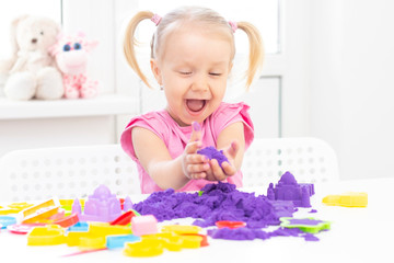 happy Girl plays kinetic sand in quarantine. Blond beautiful girl smiles and plays with purple sand...