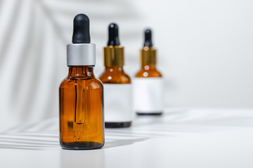 Creative photo of cosmetic bottle with pipette on a white background with shadow of tropical flower. Advertising