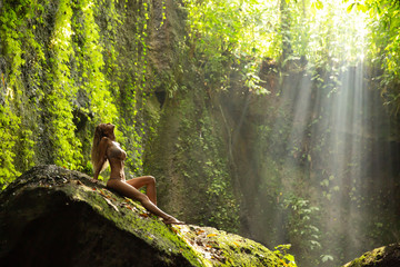 Cute girl with perfect body line in amazing landscape with light green gorge wide angle shot woman posing on a huge stone in Bali Indonesia
