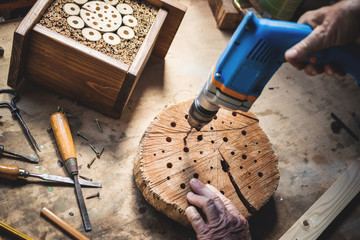 Craftsperson making wooden insect house. Carpenter using drill in workshop