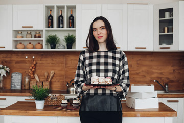 Picture of beautiful caucasian female with short dark hair in black and white sweater holds a box with marshmallows