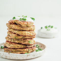 Zucchini fritters. Traditional zucchini fritters in stack on white background. Zucchini pancakes or fritters with green onion and parmesan cheese,served sour cream or greek yogurt. Copy space for text