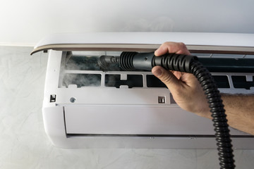 worker's hand holds brush from  portable steam generator for maintenance air condition split system, steaming for protection against dust, allergens, dirty air, microbes, healthcare concept